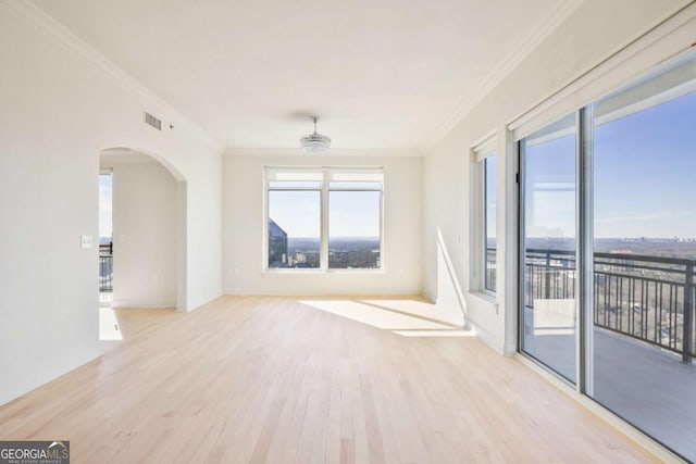 unfurnished room featuring arched walkways, wood finished floors, visible vents, and crown molding