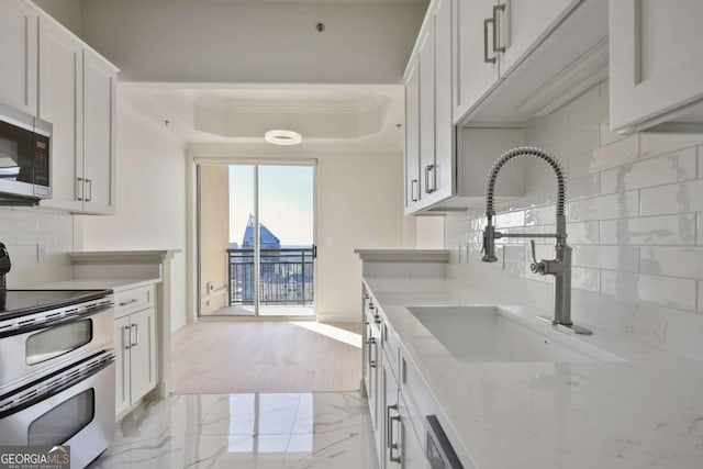 kitchen with sink, white cabinetry, light stone counters, a tray ceiling, and stainless steel appliances