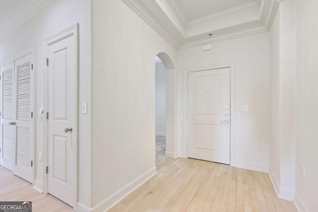 corridor featuring ornamental molding, a tray ceiling, and light wood-type flooring