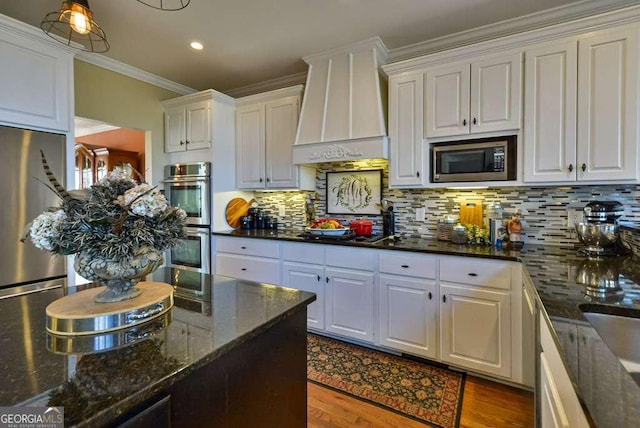 kitchen with custom exhaust hood, white cabinetry, appliances with stainless steel finishes, and ornamental molding