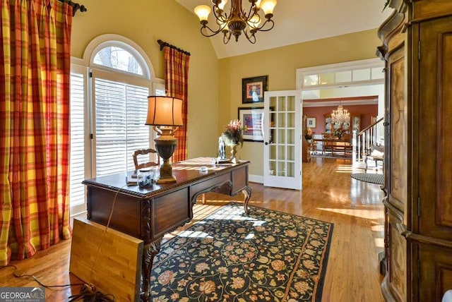 home office with an inviting chandelier, light hardwood / wood-style floors, vaulted ceiling, and french doors