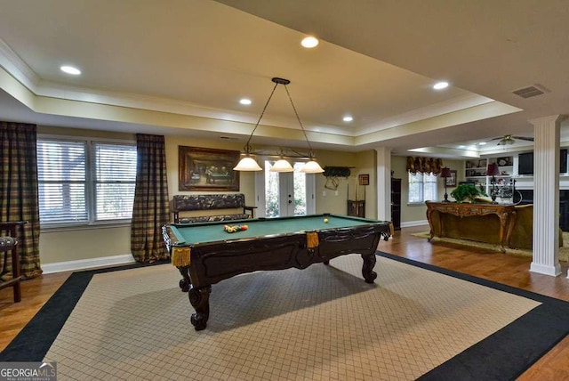 recreation room with a raised ceiling, wood-type flooring, ornamental molding, and decorative columns