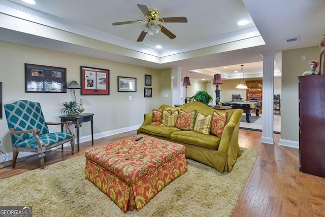 living room featuring hardwood / wood-style flooring, ornamental molding, a tray ceiling, and ornate columns