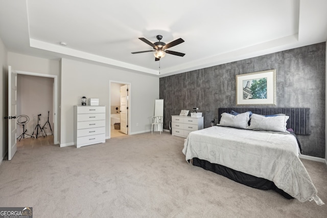 bedroom with light carpet, connected bathroom, a tray ceiling, and ceiling fan