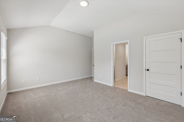 unfurnished bedroom with ensuite bath, vaulted ceiling, and light carpet