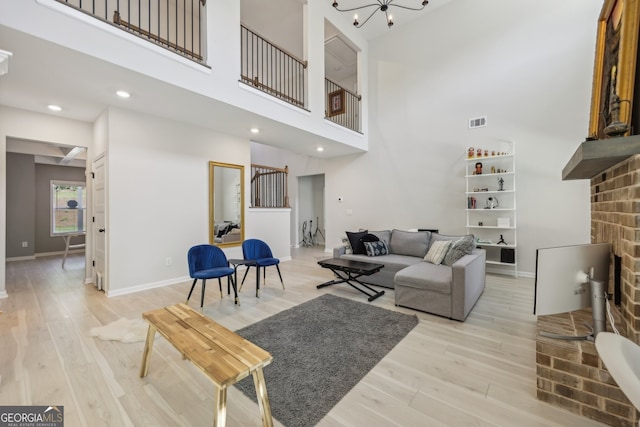 living room featuring a high ceiling, an inviting chandelier, a fireplace, and light hardwood / wood-style floors