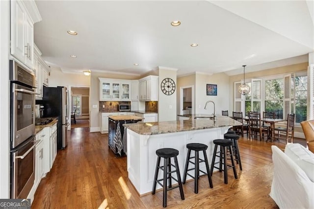 kitchen featuring appliances with stainless steel finishes, white cabinetry, sink, dark stone countertops, and a center island with sink