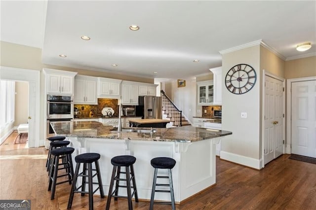 kitchen featuring white cabinetry, stainless steel appliances, a large island with sink, and a kitchen bar