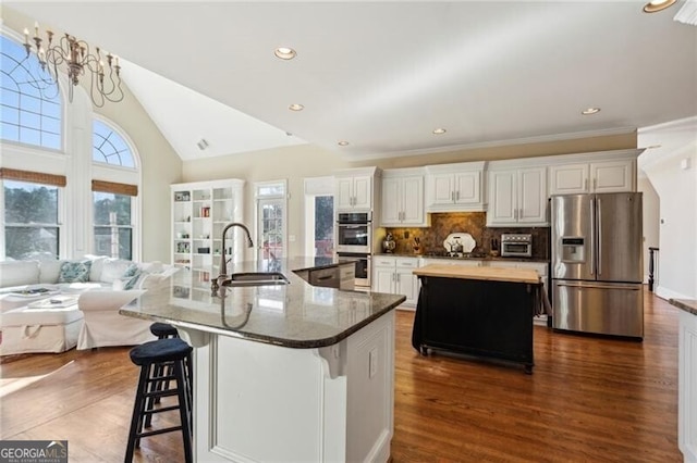 kitchen with sink, appliances with stainless steel finishes, a kitchen breakfast bar, white cabinets, and a large island with sink