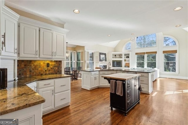 kitchen featuring vaulted ceiling, white cabinetry, a kitchen island, and kitchen peninsula