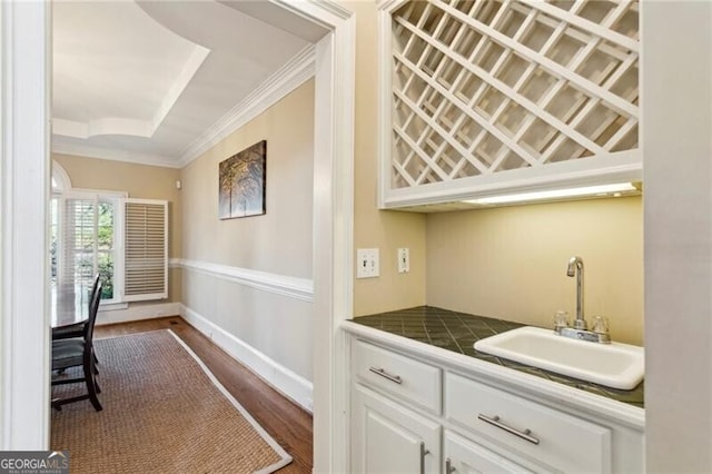 bar with dark wood-type flooring, sink, white cabinetry, crown molding, and tile countertops