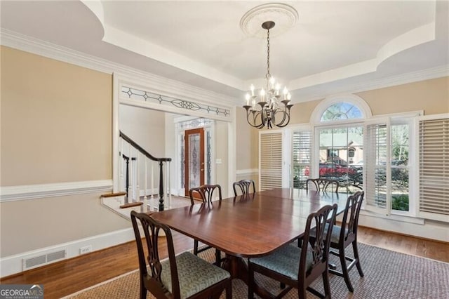 dining room featuring hardwood / wood-style flooring, crown molding, a raised ceiling, and an inviting chandelier