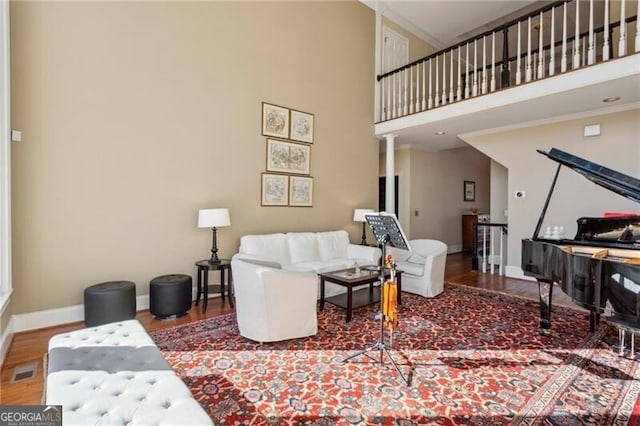 living room with crown molding, a towering ceiling, wood-type flooring, and decorative columns