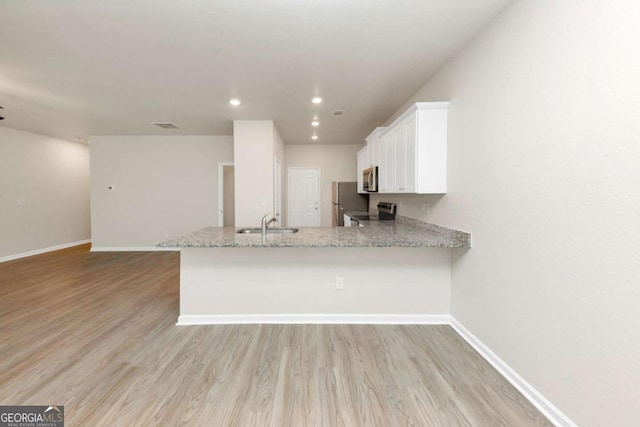 kitchen with light stone counters, appliances with stainless steel finishes, kitchen peninsula, light hardwood / wood-style floors, and white cabinets