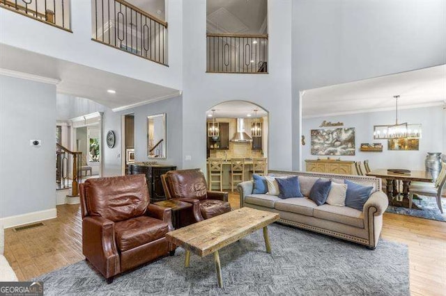 living room with crown molding, a towering ceiling, wood-type flooring, and a chandelier