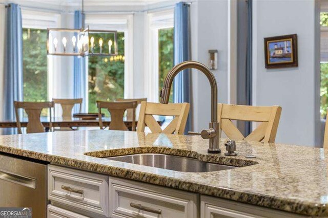 kitchen featuring white cabinetry, sink, light stone counters, and hanging light fixtures