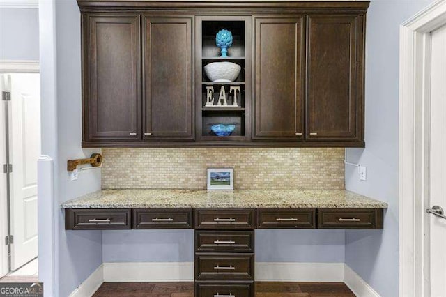 bar with dark brown cabinets, built in desk, and light stone counters