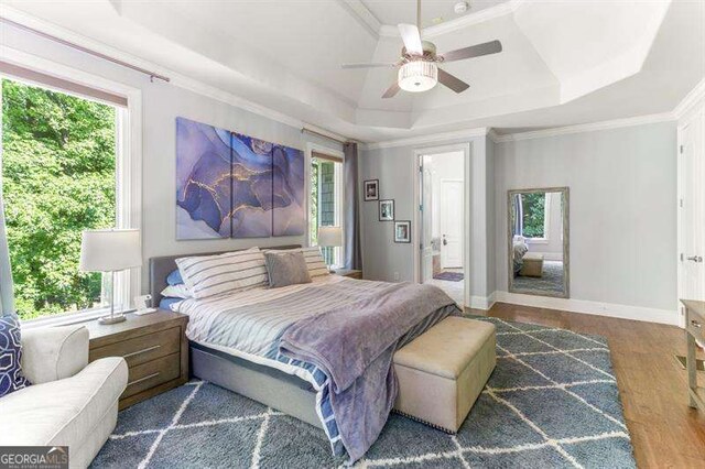 bedroom with dark hardwood / wood-style flooring, a tray ceiling, multiple windows, and ornamental molding