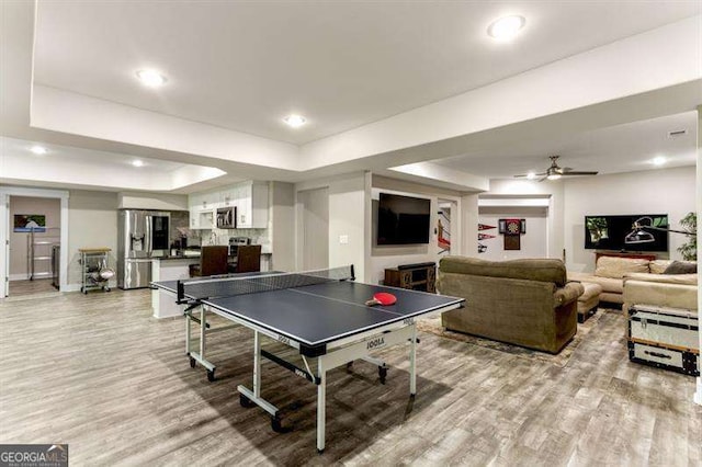 recreation room with a tray ceiling, light hardwood / wood-style floors, and ceiling fan