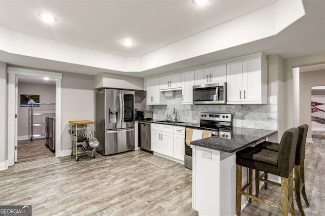 kitchen featuring white cabinets, a kitchen bar, independent washer and dryer, kitchen peninsula, and stainless steel appliances