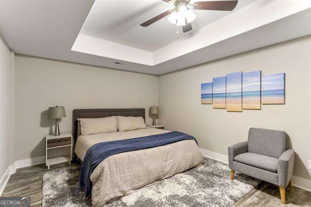 bedroom with hardwood / wood-style floors, a raised ceiling, and ceiling fan