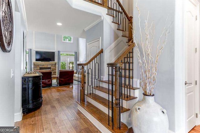 stairway with ornamental molding, a stone fireplace, and hardwood / wood-style floors