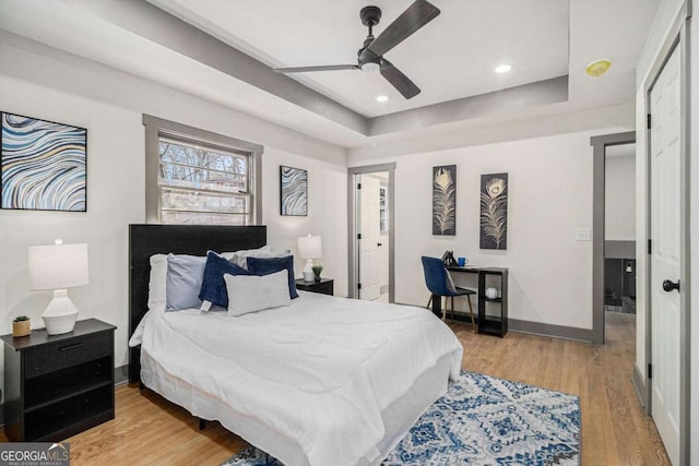 bedroom with ceiling fan, light hardwood / wood-style floors, and a tray ceiling