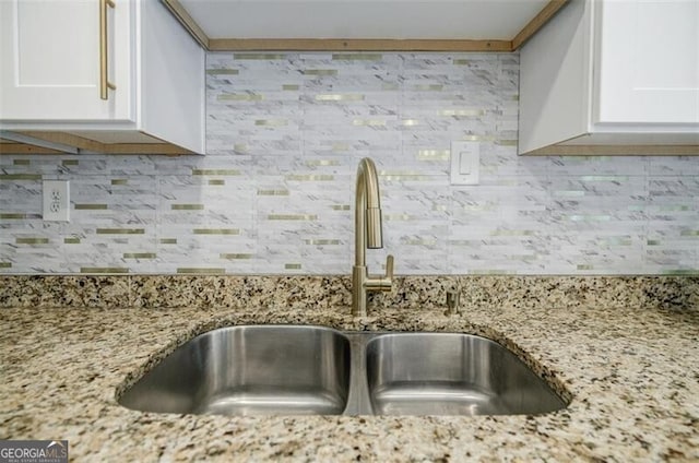 interior details with tasteful backsplash, sink, light stone counters, and white cabinets