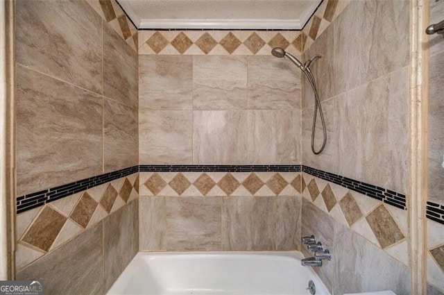 bathroom with a textured ceiling, ornamental molding, and tiled shower / bath