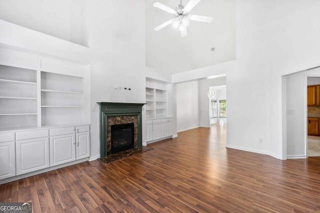 unfurnished living room with a premium fireplace, ceiling fan, dark hardwood / wood-style flooring, and built in shelves