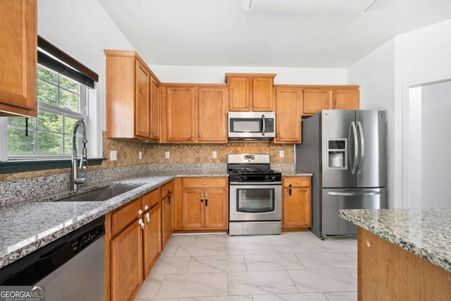 kitchen featuring tasteful backsplash, stainless steel appliances, light stone countertops, and sink