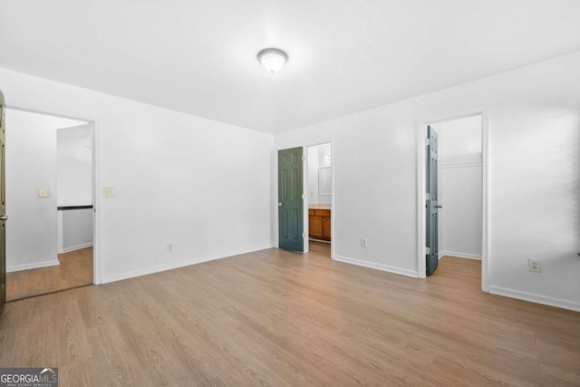 unfurnished bedroom with a walk in closet, connected bathroom, a closet, and light hardwood / wood-style flooring