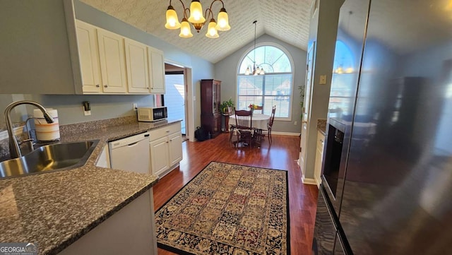 kitchen with sink, dishwasher, white cabinets, vaulted ceiling, and a chandelier