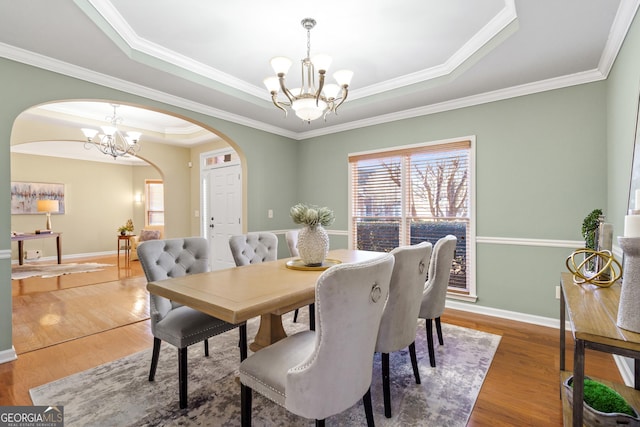 dining space with a raised ceiling, crown molding, hardwood / wood-style floors, and an inviting chandelier