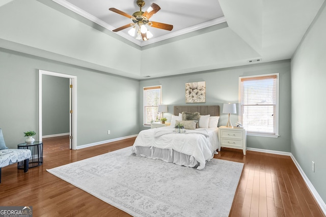 bedroom with ceiling fan, wood-type flooring, a raised ceiling, and multiple windows