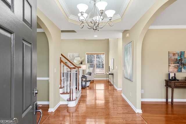 entrance foyer with crown molding, hardwood / wood-style floors, a tray ceiling, and a notable chandelier