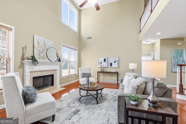 living room featuring ceiling fan, a towering ceiling, a fireplace, and light hardwood / wood-style flooring