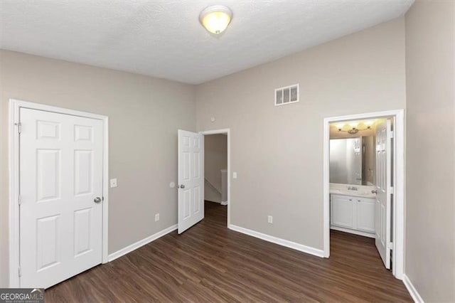 unfurnished bedroom featuring ensuite bathroom, dark hardwood / wood-style floors, sink, and a textured ceiling