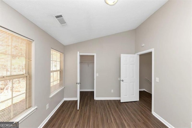 unfurnished bedroom with lofted ceiling, dark hardwood / wood-style flooring, a closet, and a spacious closet