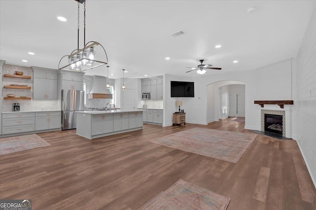 kitchen featuring pendant lighting, gray cabinetry, stainless steel appliances, dark wood-type flooring, and a center island with sink