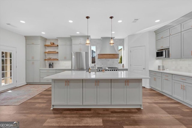 kitchen featuring stainless steel refrigerator, a kitchen island with sink, custom exhaust hood, and gray cabinetry