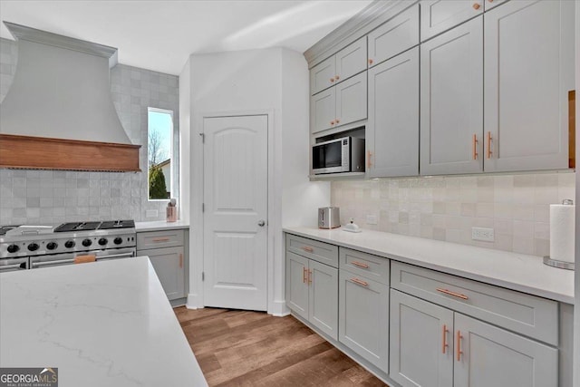 kitchen featuring gray cabinets, premium range hood, stainless steel appliances, light stone countertops, and light wood-type flooring