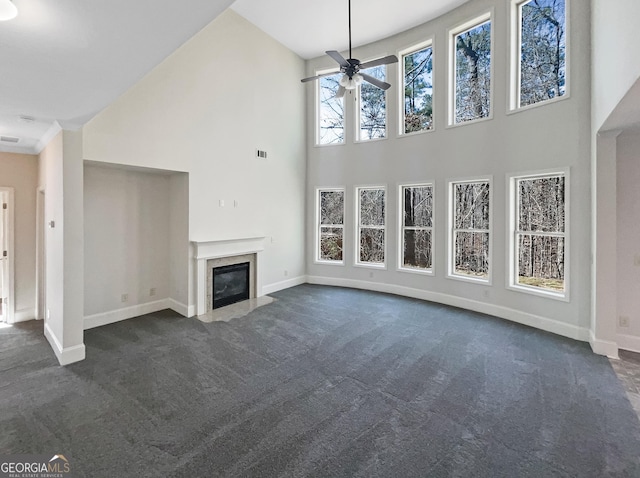 unfurnished living room with ceiling fan, a premium fireplace, a high ceiling, and dark colored carpet