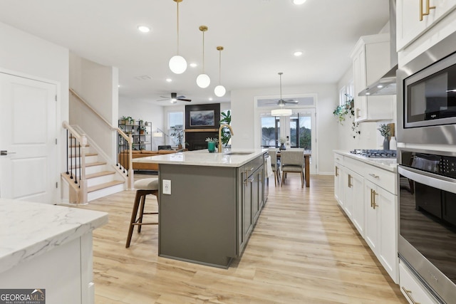 kitchen with white cabinetry, a kitchen island with sink, pendant lighting, and light stone counters