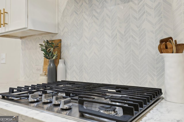 room details featuring tasteful backsplash, light stone countertops, stainless steel gas cooktop, and white cabinets