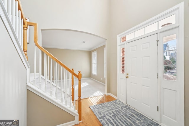 foyer with crown molding, a towering ceiling, plenty of natural light, and light wood-type flooring