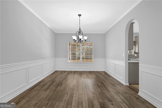 unfurnished dining area with dark wood-style floors, crown molding, arched walkways, and a notable chandelier