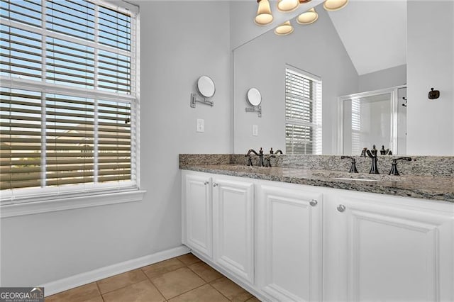 bathroom with double vanity, baseboards, tile patterned flooring, vaulted ceiling, and a sink