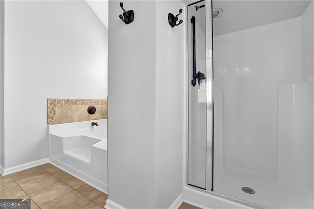 bathroom with a garden tub, a shower stall, baseboards, and tile patterned flooring