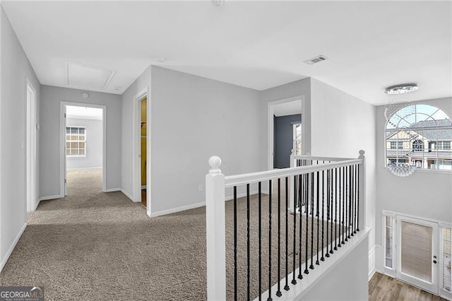 corridor with carpet floors, an upstairs landing, baseboards, visible vents, and attic access